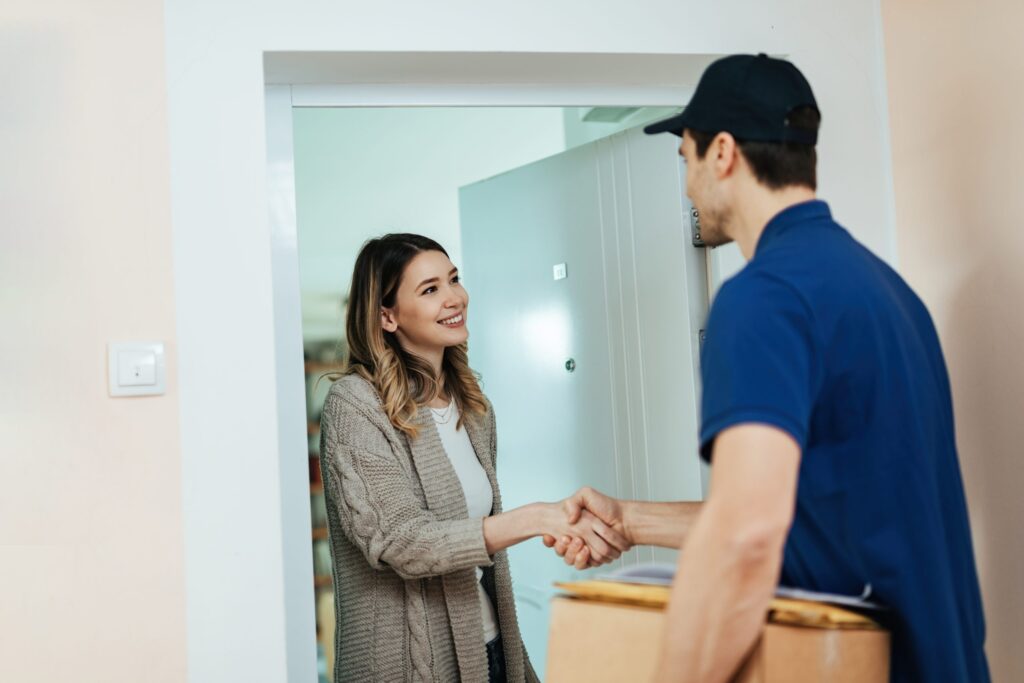 young happy woman standing doorway shaking hands with delivery man while receiving package scaled 1